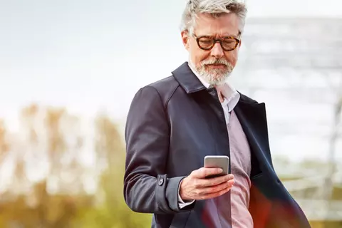 Mann mit Bart und Brille schaut auf sein Smartphone