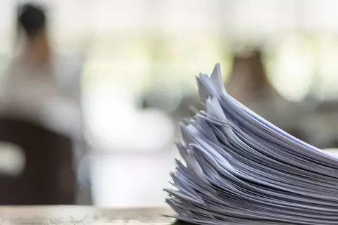 Ein großer Stapel an Papier-Unterlagen liegen auf einem Schreibtisch.