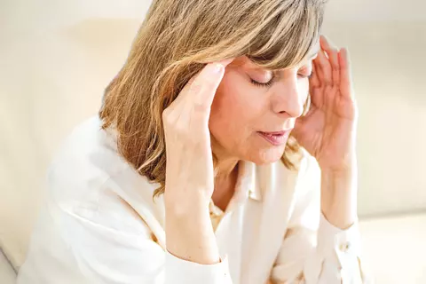 Frau sitzt aufgrund von Schwindel mit geschlossenen Augen im Wohnzimmer
