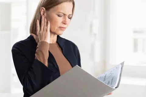 Eine Frau hält mit einer Hand eine Mappe während sie die andere Hand wegen eines Tinnitus an ihr Ohr hält