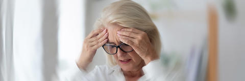 Frau mit Brille hält aufgrund von Schwindel ihren Kopf in den Händen