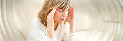 Frau sitzt aufgrund von Schwindel mit geschlossenen Augen im Wohnzimmer