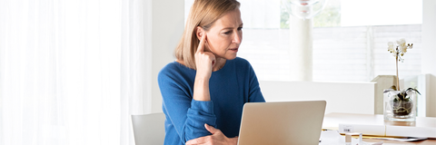 Gestresste Frau vor einem Laptop fasst sich ans Ohr